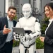 A humanoid robot sitting at a desk, working on a laptop while a woman stands beside it, smiling. This image represents AI in recruitment, emphasizing how artificial intelligence supports hiring processes and workplace automation.