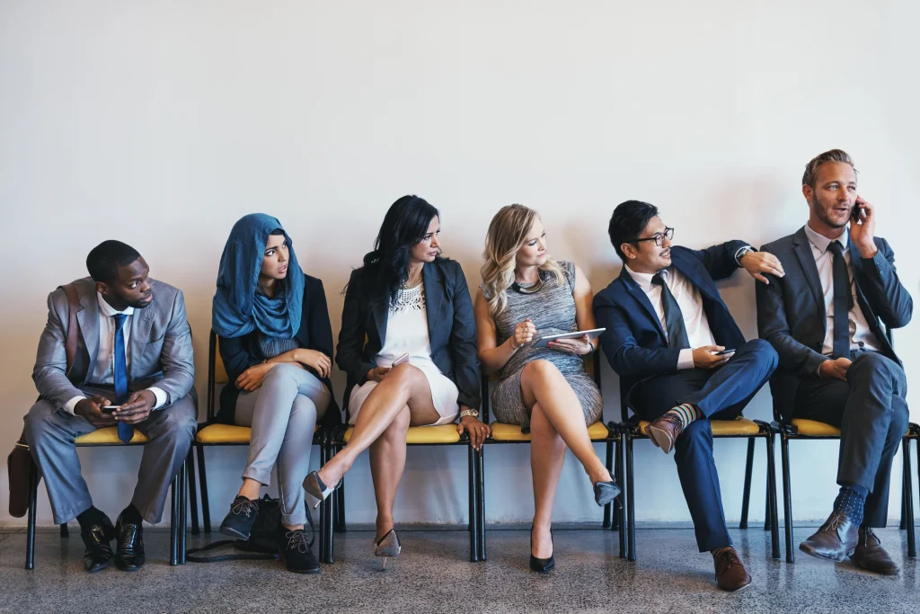 Diverse group of professionals in business attire sitting in chairs, waiting for a tech job interview