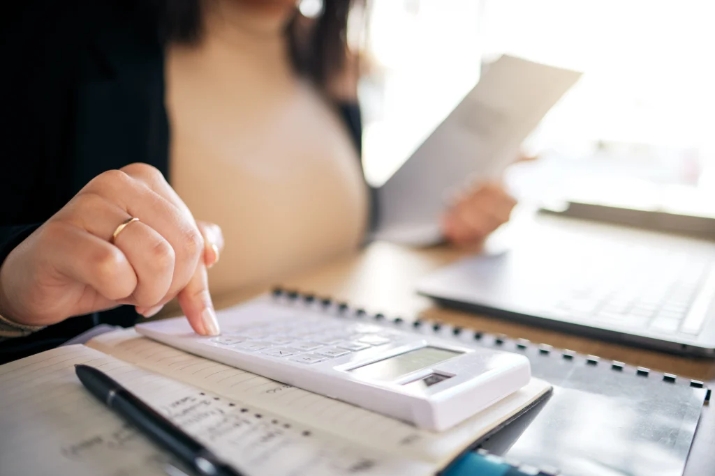 Outsourcing bookkeeping and taxation depicted by an accountant using a calculator, taking notes, and reviewing documents at a modern workspace.