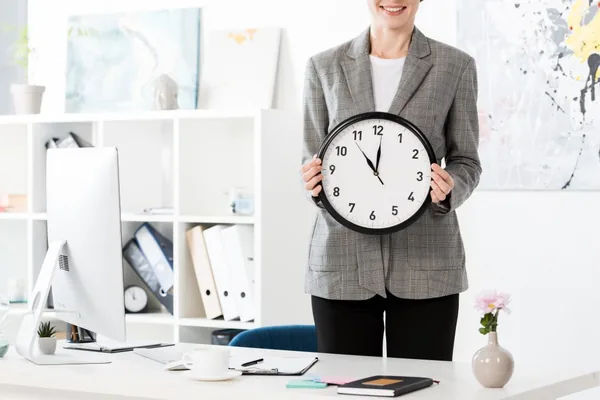 cropped image of attractive businesswoman holding wall clock in office portraying a full time employee
